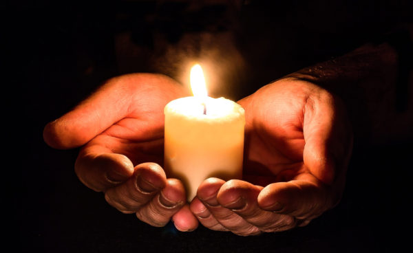 a lit candle cupped in two hands, glowing.