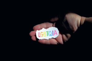 A hand holding a small paper sign with "LGBTQIA" written in rainbow colours. 