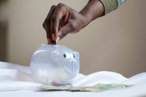 A hand putting a coin into a translucent piggy bank.