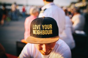 A person wearing a ball cap with the words "Love your neighbour"