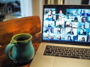 A laptop with faces in squares on the screen. A blue pottery mug sits by the keyboard.