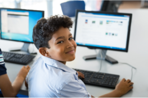 A child looking over their shoulder with an awesome grin as they work at a computer.