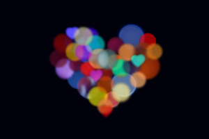 Rainbow coloured heart made of circles of light of all colours, on a black background.