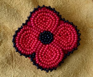 A red and black hand beaded poppy set on a buckskin background.