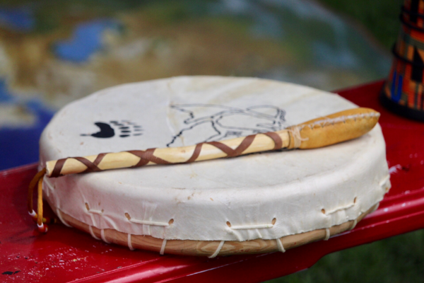 A traditional hide drum and drumstick with black painted designs.