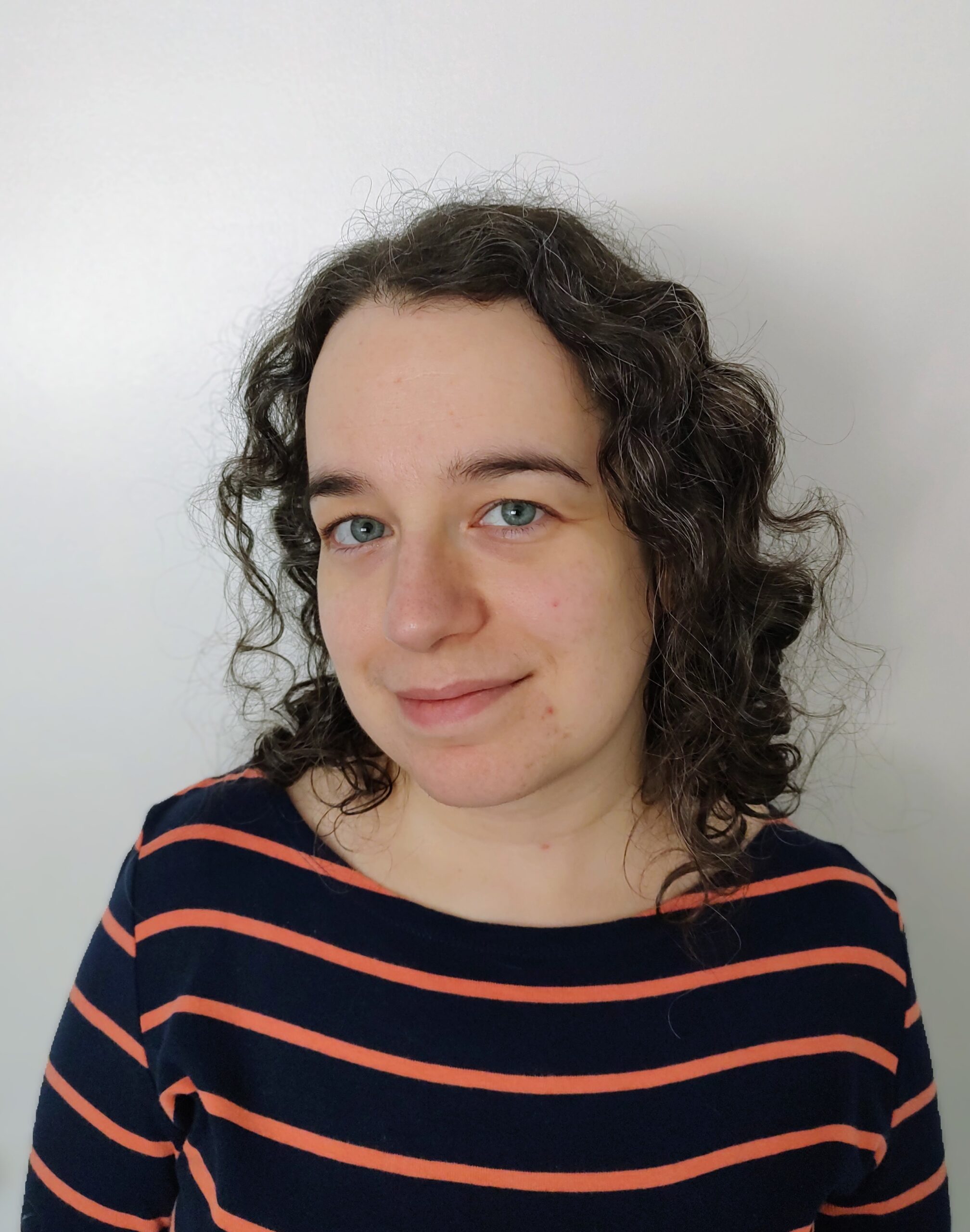 A woman with dark curly hair and a blue and red shirt smiling into the camera.